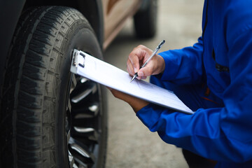 Auto mechanic is writing on clipboard. Mechanic is making checklist and checking condition of car tire. Concept of car service, repair, maintenance.