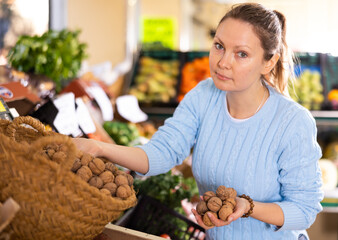 Portrait of busy middle-aged European woman in casual wear buying walnuts in shell in grocery store