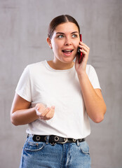 Amazed young woman talking on mobile in bewilderment against paly monochromatic background