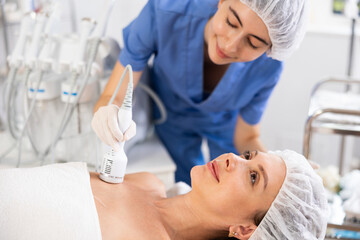 Young woman undergoing hardware treatment of collarbones area using cold hammer helping to shrink...