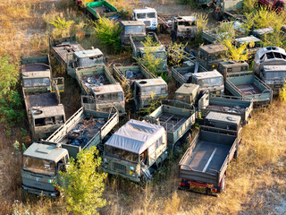Aerial view of a truck graveyard where old military trucks rest among tall grasses, a scene of decay in the open air, Pinerolo, Piedmont, Italy.