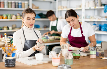 Fototapeta premium Two young women in apron modeling clay pottery in workshop