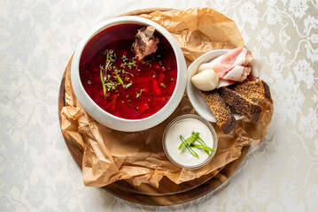 Rustic serving of traditional borscht soup with bone, herbs, rye bread, garlic, bacon, and sour...