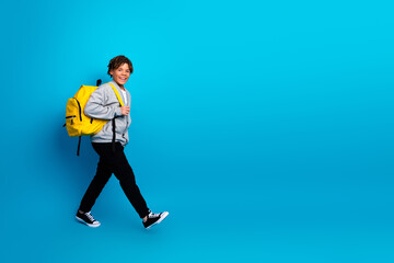 Smiling schoolboy with a yellow backpack walking confidently against a blue background, showcasing...