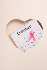 An October calendar lies within a vertical heart frame, featuring a pink ribbon, symbolizing breast...