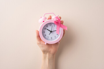 Pink alarm clock held in hand adorned with a symbolic pink ribbon and simple background