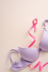Pink ribbon and a purple bra lying on a vertical beige background, symbolizing breast cancer...