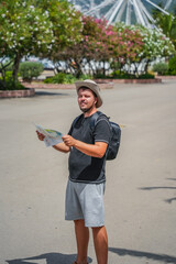 Man in hat with backpack looking at map outdoors, travel and exploration