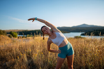 Relaxed young woman stretching outdoors in summer by the lake