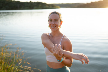 Sportswoman stretching arms by the lake during summer workout
