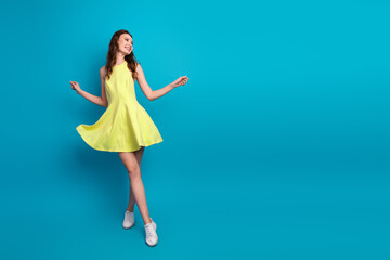 Stylish young woman in a yellow dress posing against a vibrant blue background, showcasing trendy fashion and glamour