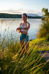 Sporty woman wearing running sunglasses checking her smartwatch during an outdoor summer workout by...