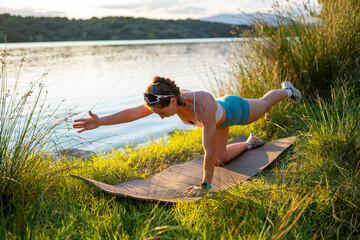 Young woman performing bird-dog exercise by the lake at sunset