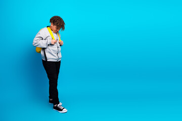 Young student with backpack in casual grey cardigan poses against a blue background, symbolizing...