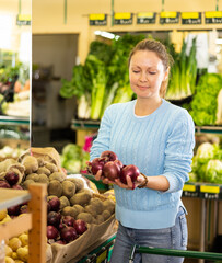 in modern supermarket, woman carefully selects onions and puts them in shopping cart