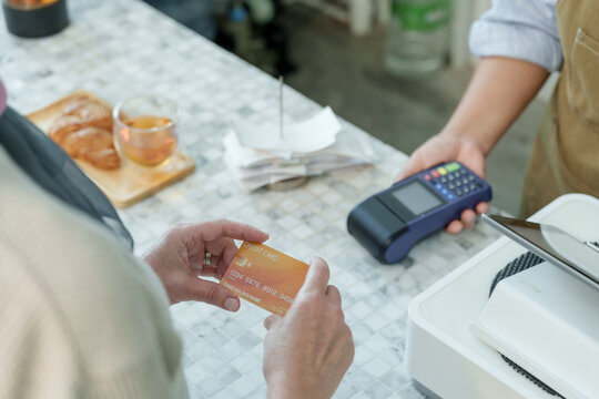 Customer holding orange credit card preparing for payment at cafe counter reflecting readiness for cashless transaction in cozy small family coffee shop