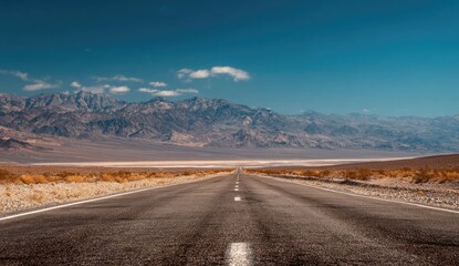 Empty road stretching into a vast desert landscape, mountains rise in the distance under a clear blue sky