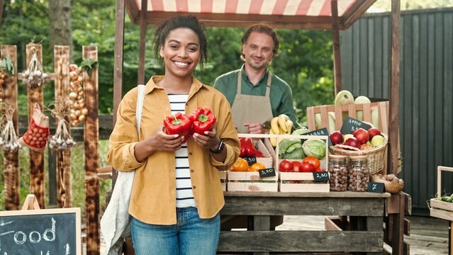 African American woman outdoor buying food at food market. Woman buy vegetables and paying with smartphone pay pass. Male and female family of farmers work at market selling organic products