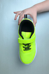 Light green sneakers in hands on a gray background.