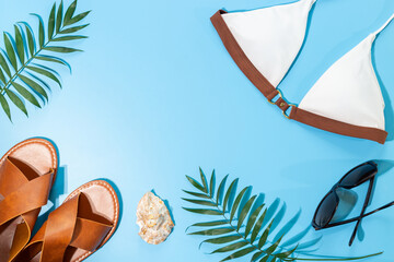 Vacation beach accessories with sunlight shadows. Stylish bikini swimsuit with sandals and tropical leaves, top view