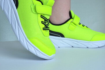 Light green sneakers with white soles and black laces on the feet. Gray background.