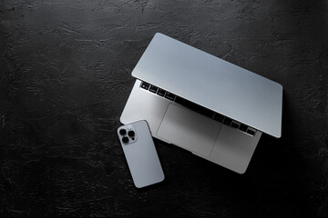 Silver laptop and mobile phone - high tech gadgets - on black stone background, top view