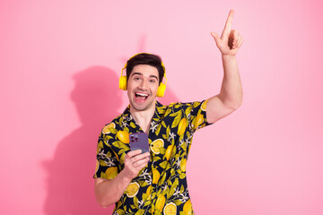 Cheerful man in vibrant tropical shirt enjoying music with gesture on pink background - young...