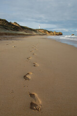 Footprints lead down a sandy beach towards Split Point Lighthouse, a navigational aid guiding ships along the Victorian coastline.