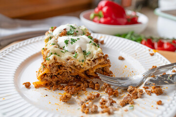 Homemade enchilada filled with ground beef and topped with cheese and sour cream on a plate