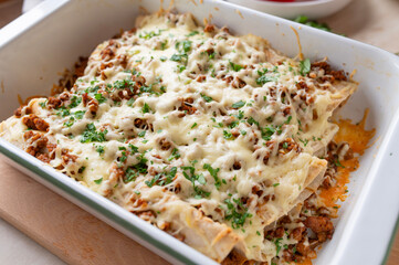 Homemade enchiladas in a white baking pan filled with minced meat and topped with cheese