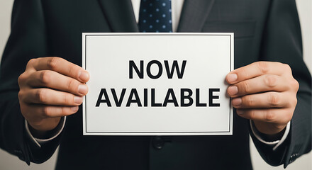 Obraz premium Man in Suit Holding Now Available Sign image