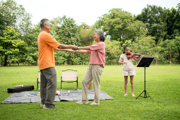 Happy Asian grandparents enjoying a picnic with their granddaughter in a green park
