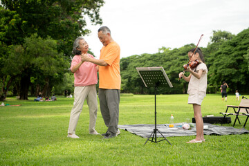 Happy Asian grandparents enjoying a picnic with their granddaughter in a green park