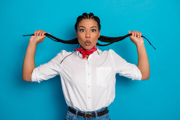 Young woman with braided hair holding her braids playfully against a vibrant blue background in...