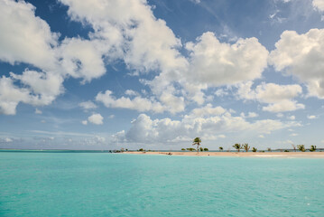 A scenic view of a tropical island with turquoise waters and a sandy beach, dotted with palm trees, under a partly cloudy sky, creating a serene and inviting atmosphere.
