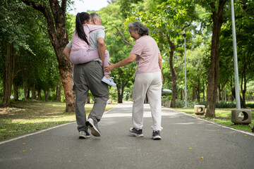 Fototapeta premium Happy Asian grandparents and granddaughter running joyfully together in a park