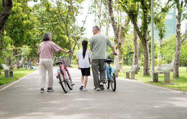Happy Asian grandparents walking with bicycles alongside their granddaughter in a park