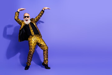 Stylish elderly gentleman in a golden patterned suit dancing against a violet background with...