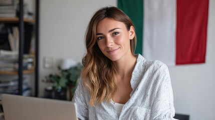 An Italian teacher at a table with a laptop in front of the Italian flag preparing for an online lesson