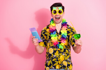 Joyful young man with tropical attire in colorful lei holding a drink and paper on vibrant pink...