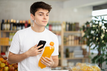 Guy customer at shop scan QR code on drink bottle using phone camera. Client inspect item,...