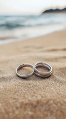 Two Silver Wedding Rings on Sandy Beach with Ocean Blur in Soft Light
