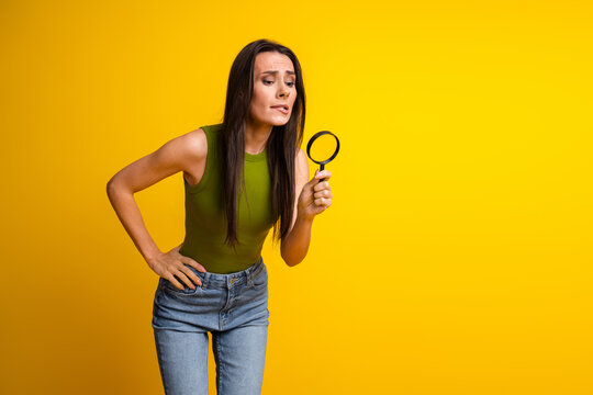 Woman in green top with magnifying glass poses thoughtfully against yellow background symbolizing curiosity and focus