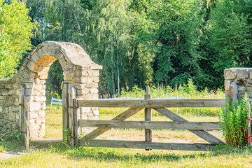 Ancient brick archway with wooden gate in a lush, vegetated Central European village setting...