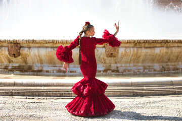 A beautiful woman dancing flamenco in a square in Seville, Spain. She is wearing a red dress with...