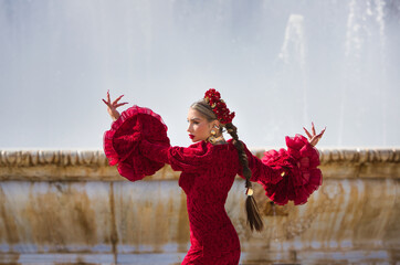 A beautiful woman dancing flamenco in a square in Seville, Spain. She is wearing a red dress with...
