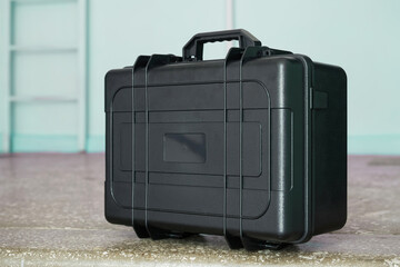 Durable black hard case with secure latches, designed for ultimate protection of sensitive equipment, tools, or fragile items, standing on a textured floor. Photo