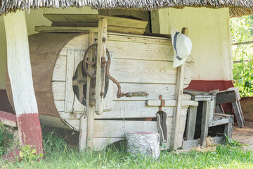 An old wooden cart with a barrel on a grassy village ground Disarrayed items nearby cardboard...