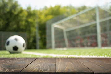Empty wooden table top and blurred soccer field with ball. Summer leisure activity. Abstract football background for design.
