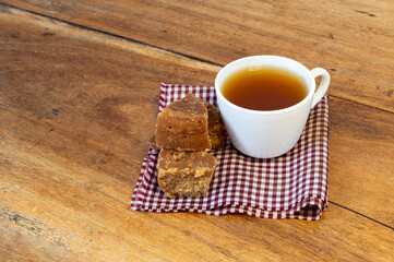 Aguapanela, Agua de Panela or Aguadulce in a white glass, popular Latin American sweet drink, with pieces of panela on a wooden table
